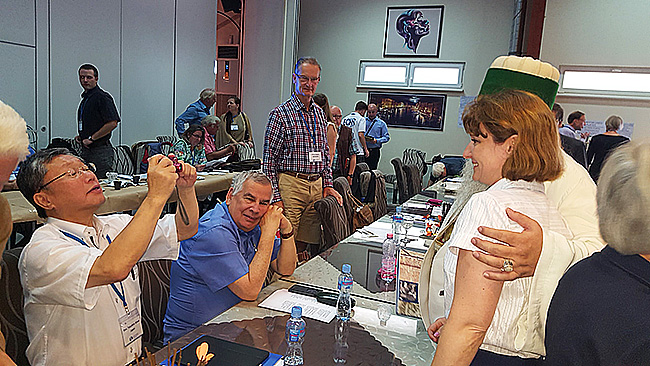 Conference participants greeting one another and taking photographs around the meeting tables.