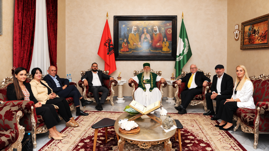 Robert Ince, Baba Mondi and other participants sit together between the Albanian and Bektashi flags.